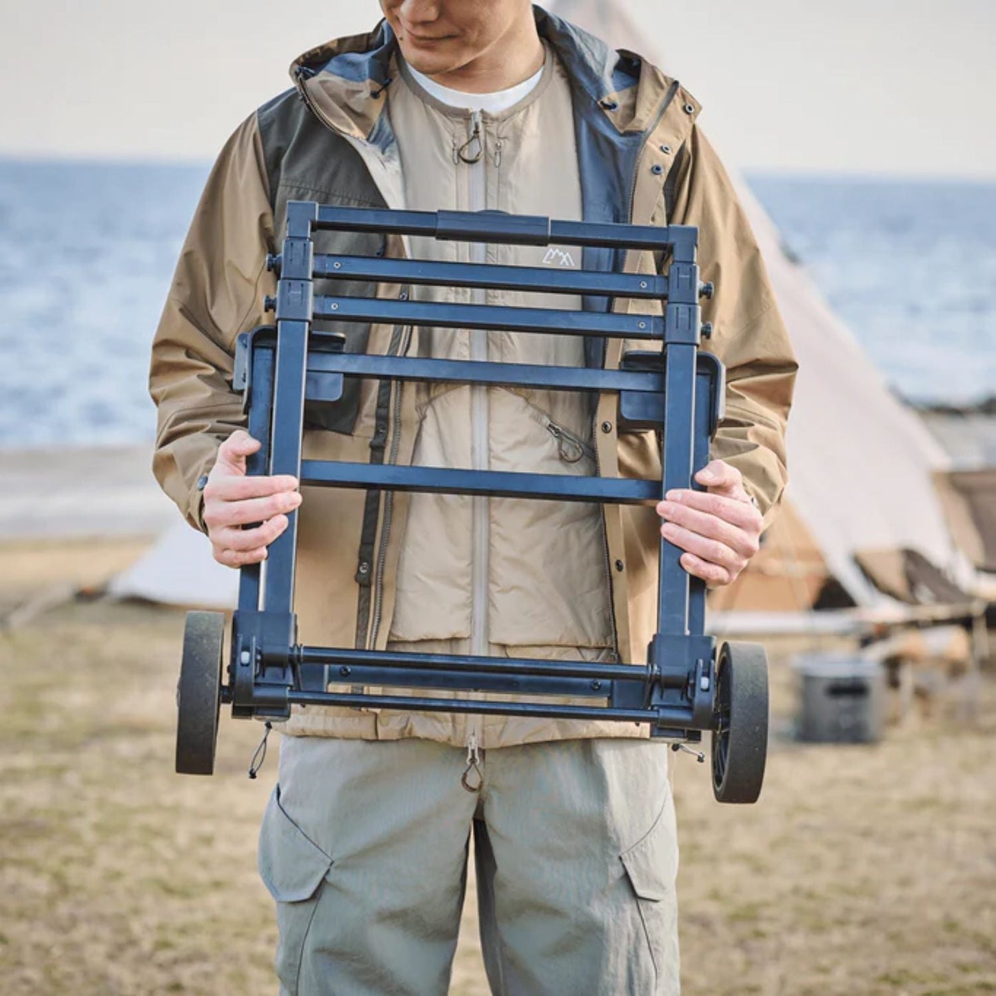 Person holding a Jackery Power Station Trolley on a beach with tents 