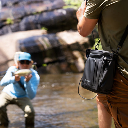 Two people fishing by a river with one person holding a fish and the other wearing EcoFlow TRAIL 200DC Portable Power Station